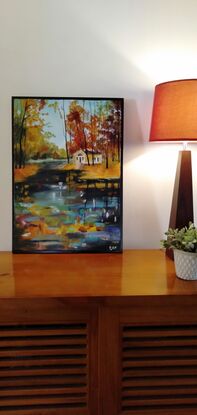 A beautiful brightly coloured painting showing a cabin in the woods by a flowing stream.