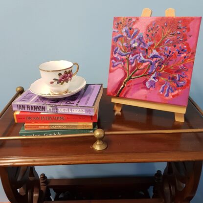 A stem of Jacaranda flowers, a three pronged branch showing purple and mauve trumpet shaped blossoms against a pink and red background.