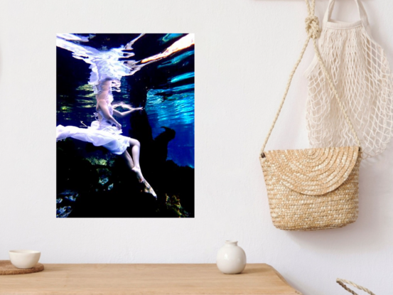 Young woman sitting on a log underwater in white dress whilst creating reflections in the surface.