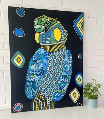 Black cockatoo painted in blues greens and yellows looking directly at the viewer. Painted on a dark navy background with yellow diamond shapes