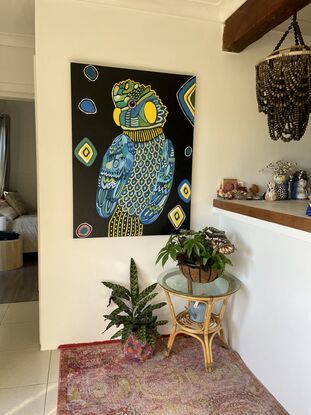 Black cockatoo painted in blues greens and yellows looking directly at the viewer. Painted on a dark navy background with yellow diamond shapes