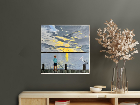 A boy fishing next to the river while a pelican watches.