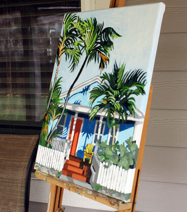 Florida-style beach house surrounded by palm trees and a picket fence and a yellow chair.