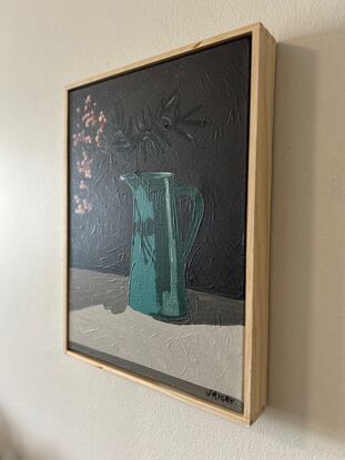 A tall deep aqua coloured vintage jug sits on a sideboard. In it are bare branches with berries light red in colour. They cast a shadow on the jug and the background is a dark grey.