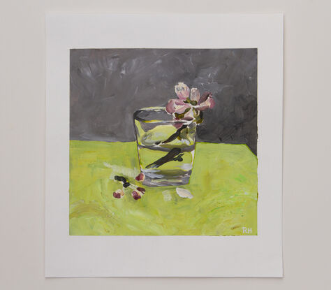 This is a single cherry blossom, in a glass of water, painted on a bench of bright green, with a grey backdrop.