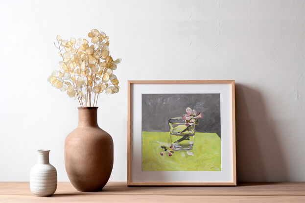 This is a single cherry blossom, in a glass of water, painted on a bench of bright green, with a grey backdrop.