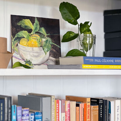 Three yellow lemons and their leaves in a white ceramic bowl on a white linen tea towel, with a beautiful red and blue stripe