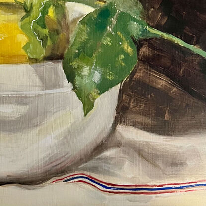 Three yellow lemons and their leaves in a white ceramic bowl on a white linen tea towel, with a beautiful red and blue stripe