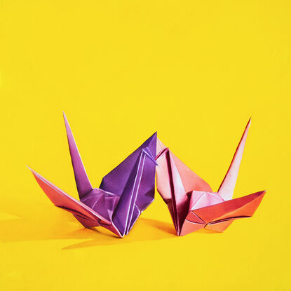 Two origami cranes sharing a kiss against a yellow background