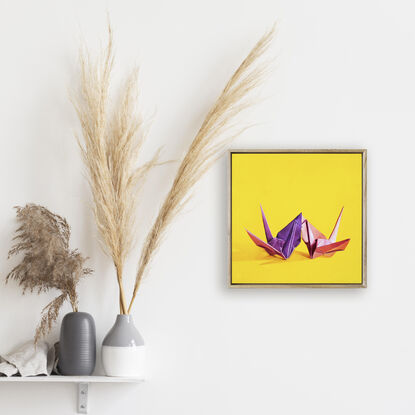 Two origami cranes sharing a kiss against a yellow background