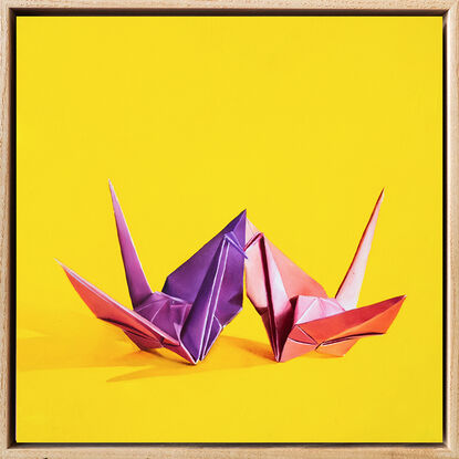 Two origami cranes sharing a kiss against a yellow background