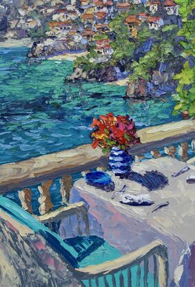 Teal chairs bask in the sun invite the viewer to take in the seaside view from the table on the cliffs above Portofino.  A vase of flowers, plates and napkins are on a white tablecloth.