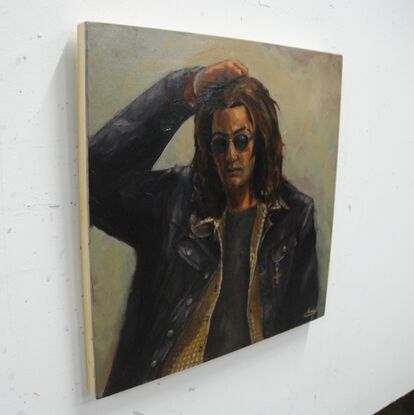 A portrait of a person with shoulder length curly brown hair, wearing sunglasses and a denim jacket with a flannel shirt over a grey t-shirt. There is a green synthetic glow to the lighting and the figure's posture seems tired and frustrated. By H. Fleming