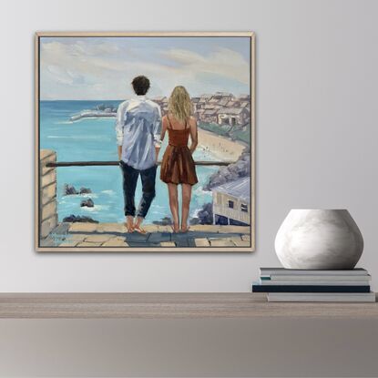 A young couple looking out to sea. He with dark hair, wearing  a white linen shirt. She with blonde hair and a warm brown dress.