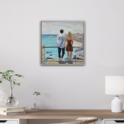 A young couple looking out to sea. He with dark hair, wearing  a white linen shirt. She with blonde hair and a warm brown dress.