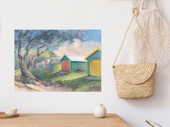 Colourful timber beach sheds with grass and sand and a large twisting tree in foreground.