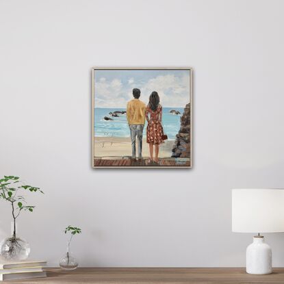 A young couple looking out to sea. He with dark hair, wearing  a white linen shirt. She with blonde hair and a warm brown dress.