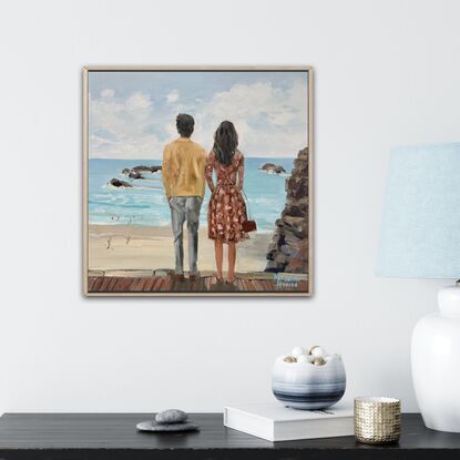 A young couple looking out to sea. He with dark hair, wearing  a white linen shirt. She with blonde hair and a warm brown dress.