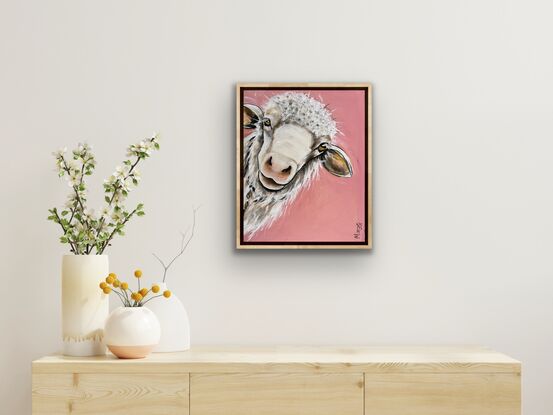 A young sheep with an inquisition expression staring out from the canvas with a peach pink background.