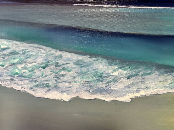 A clear night with the moon peeping from behind clouds and reflected on waves and wet sand.