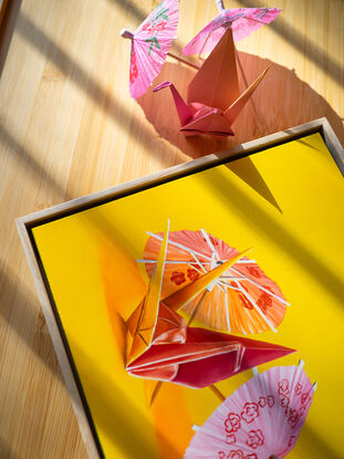 An origami bunny standing amongst cocktail parasols against a yellow background