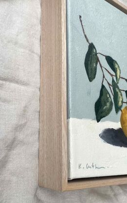 A lemon on a branch with leaves painted with subtle texture on a cream base and a blue grey background