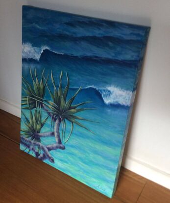 Pandanus palm with sunlit leaves and curving branches, reaching out over the curling waves in the aqua ocean below.