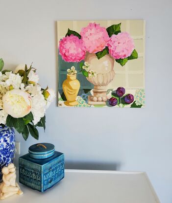 A Serene Still Life of 3 Pink Hydrangeas in a neutral toned terracotta Urn with 3 plums on patterned fabric.