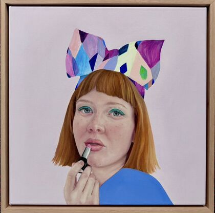 A beautiful red headed girl with bright green eyeshadow  and rosy cheeks is applying a peach colour lipstick. She is wearing an amazingly colourful and quirky headband with a big bow. She is dressed in colbolt blue and is posed against a lilac background.