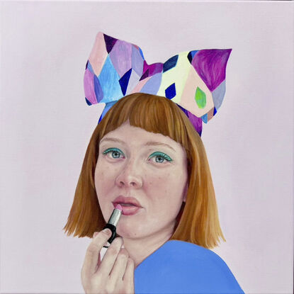 A beautiful red headed girl with bright green eyeshadow  and rosy cheeks is applying a peach colour lipstick. She is wearing an amazingly colourful and quirky headband with a big bow. She is dressed in colbolt blue and is posed against a lilac background.