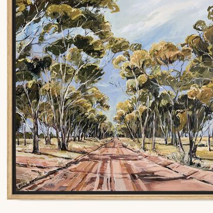 A dirt track runs between a large group of tall gum trees. A blue sky has whispers of clouds. 