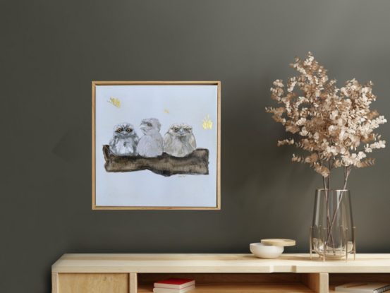 Three baby Tawny Frogmouth birds resting on a large tree branch as a golden moth flutters past. 