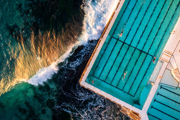 Aerial View Of Bondi's iconic pool Ice bergs at Bondi. Taken with at sunrise the golden glow hits a wave from the side. 