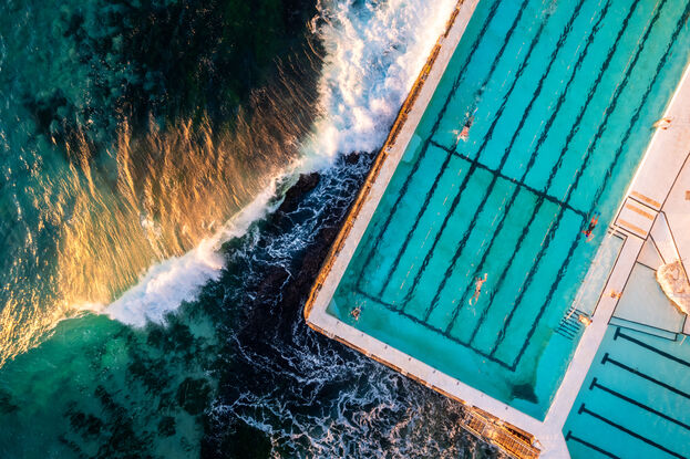 Aerial View Of Bondi's iconic pool Ice bergs at Bondi. Taken with at sunrise the golden glow hits a wave from the side. 