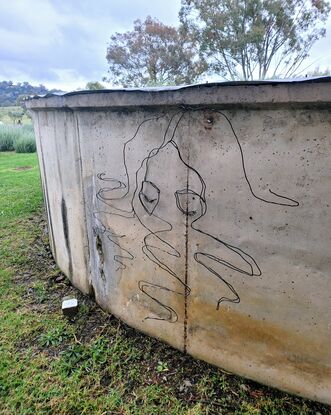 A continuous line drawing sculpture,  made with wire, of a woman with her face half submerged into water. Curls of hair floating around her. 