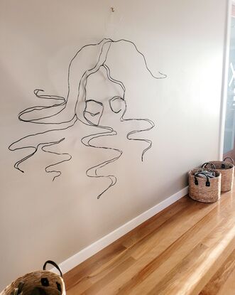 A continuous line drawing sculpture,  made with wire, of a woman with her face half submerged into water. Curls of hair floating around her. 