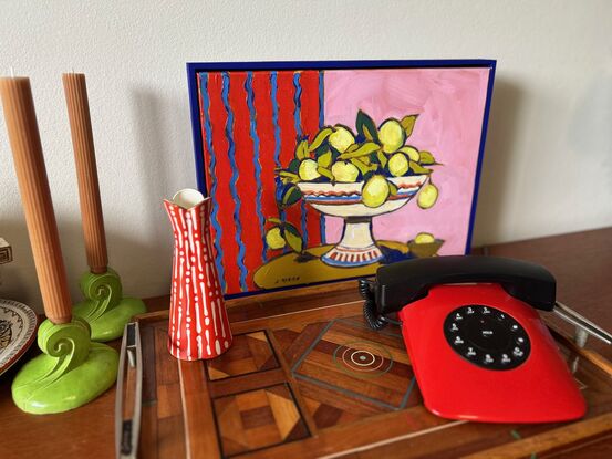 a modernist still life with bright red and pink background. A white pedestal bowl of lemons sits on a rounded brown table