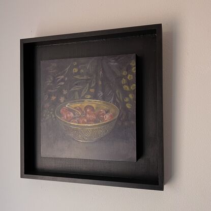 A brass bowl of grapes on a black surface with a patterned black fabric behind