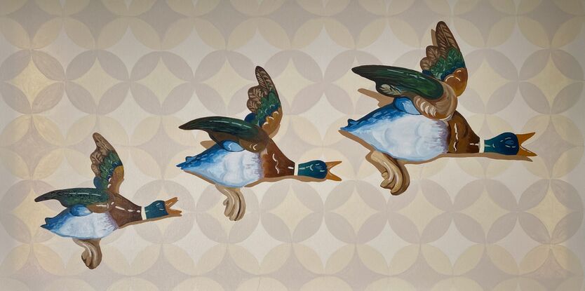 Three ceramic mallard ducks flying across a beige patterned wallpapered wall