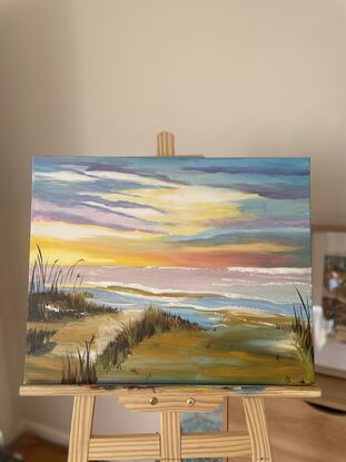 The painting is created with acrylic paints in light tones. At the middle of the canvas is a horizon line of the sea. The sun sits on this line, using the brightest of yellows to portray the suns position. then the colours blend to oranges, whites, purples and blues. The ocean reflects those colours. Ive depicted sand dunes in detail and a deep earthy wet sand colour for the bottom half of the painting. 