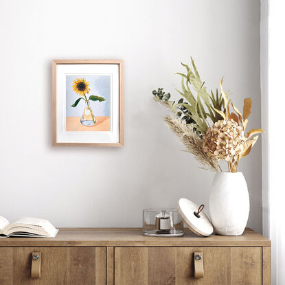 One sunflower in glass vase on peach and blue background