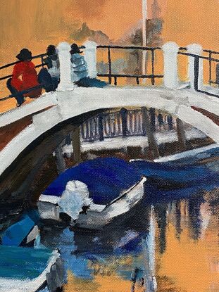 A couple of people sit with their knees on a step on a Venetian Bridge. There are a couple of boats in the water. And bright colours from the building behind them reflecting in the water.