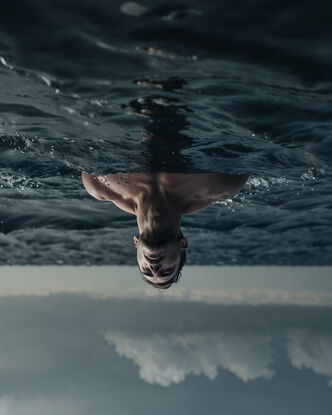 A man stands in the ocean, partially submerged, looking up into the heavens. The image has been flipped vertically.