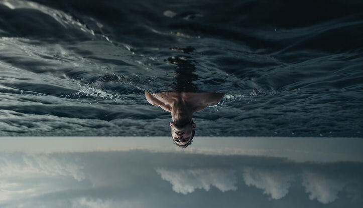 A man stands in the ocean, partially submerged, looking up into the heavens. The image has been flipped vertically.