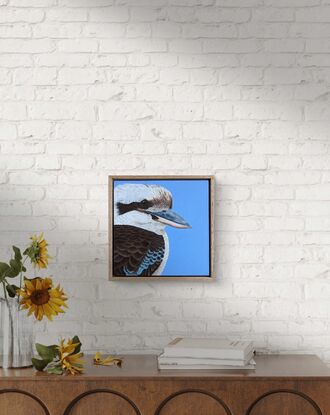 A painting of an Australian Laughing kookaburra profile and upper body against a sky blue background. Framed in Tasmanian oak.