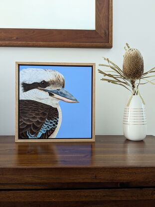 A painting of an Australian Laughing kookaburra profile and upper body against a sky blue background. Framed in Tasmanian oak.