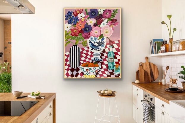 Red and white tablecloth with drink and bowl of oranges with large vase of flowers