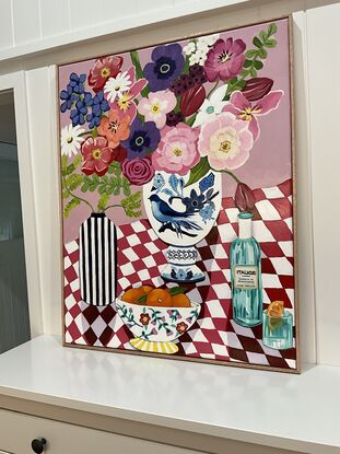 Red and white tablecloth with drink and bowl of oranges with large vase of flowers