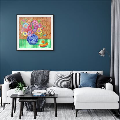 Colourful flowers in blue and white vase in front of red ochre patterned background on green checkered tablecloth with a pink plate of oranges.