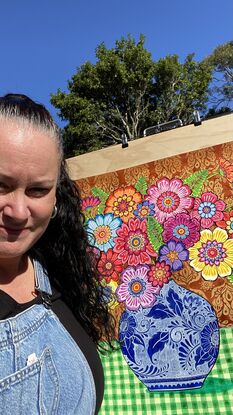 Colourful flowers in blue and white vase in front of red ochre patterned background on green checkered tablecloth with a pink plate of oranges.